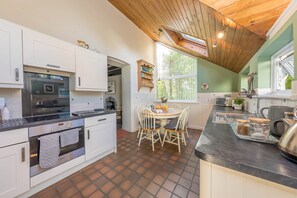 A kitchen with white cabinets, a Bosch oven, a dining table with chairs, and a window with a view of greenery.