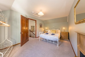 Un dormitorio con cama, mesitas de noche, un espejo y una escalera que lleva a otra habitación.