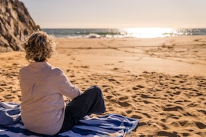 A person sitting on a beach towel facing the ocean.
