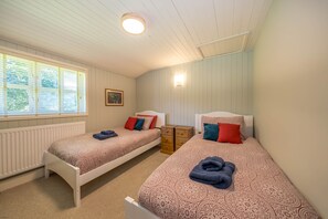 A bedroom with two single beds, a nightstand, a radiator, a window with blinds, and a ceiling light.