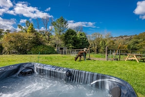 A hot tub in a grassy area with a wooden fence and trees in the background. - Ffawydd-Y-Ffynnon -  a self catering cottage that sleeps 6 guests  in 3 bedrooms (Llanfyrnach)