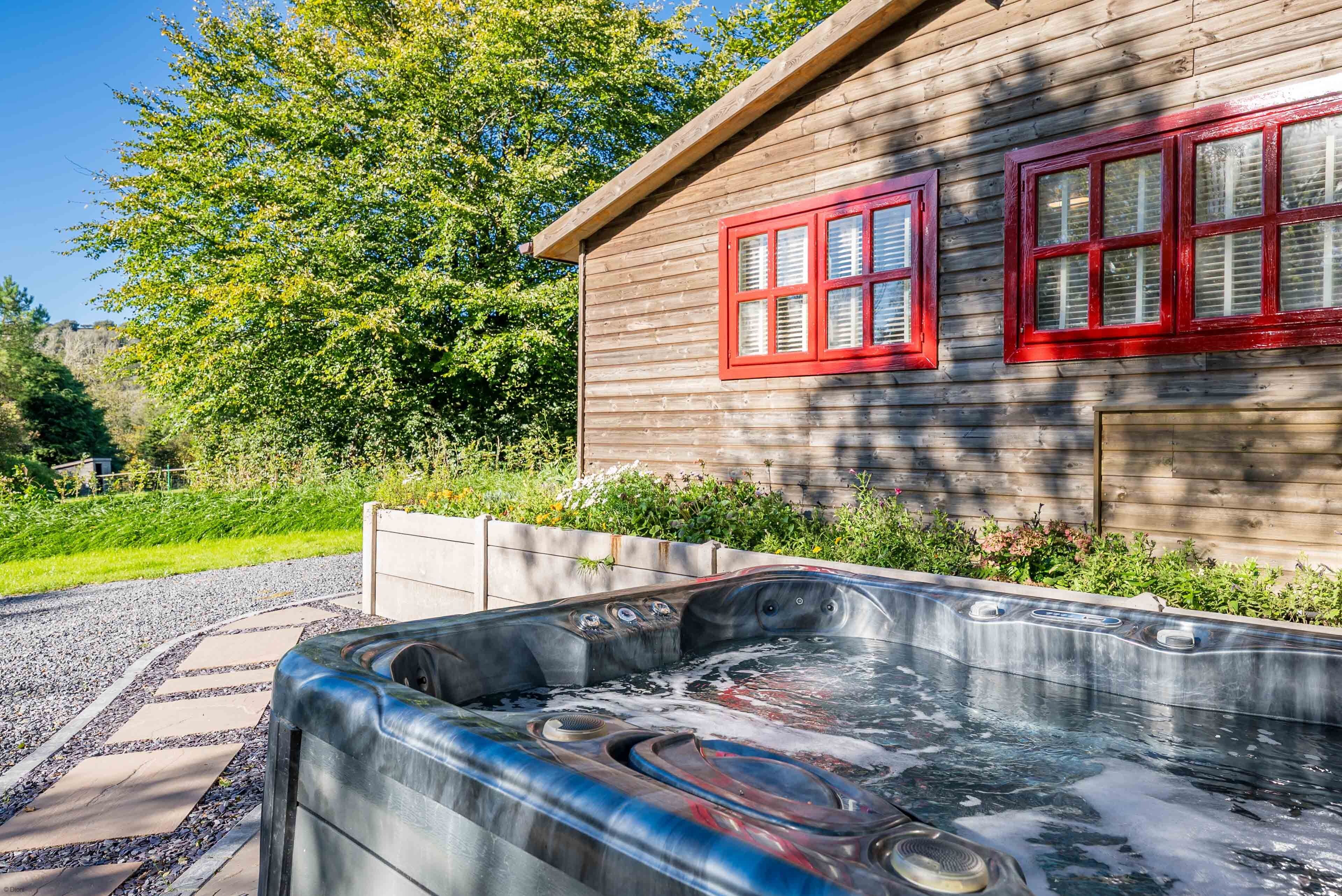Una cabaña de madera con un jacuzzi y un camino de grava que la lleva a ella.