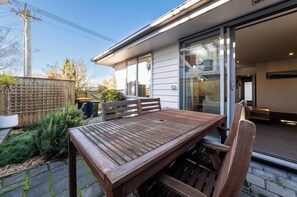 A wooden table and chairs outside a house with a sliding glass door.