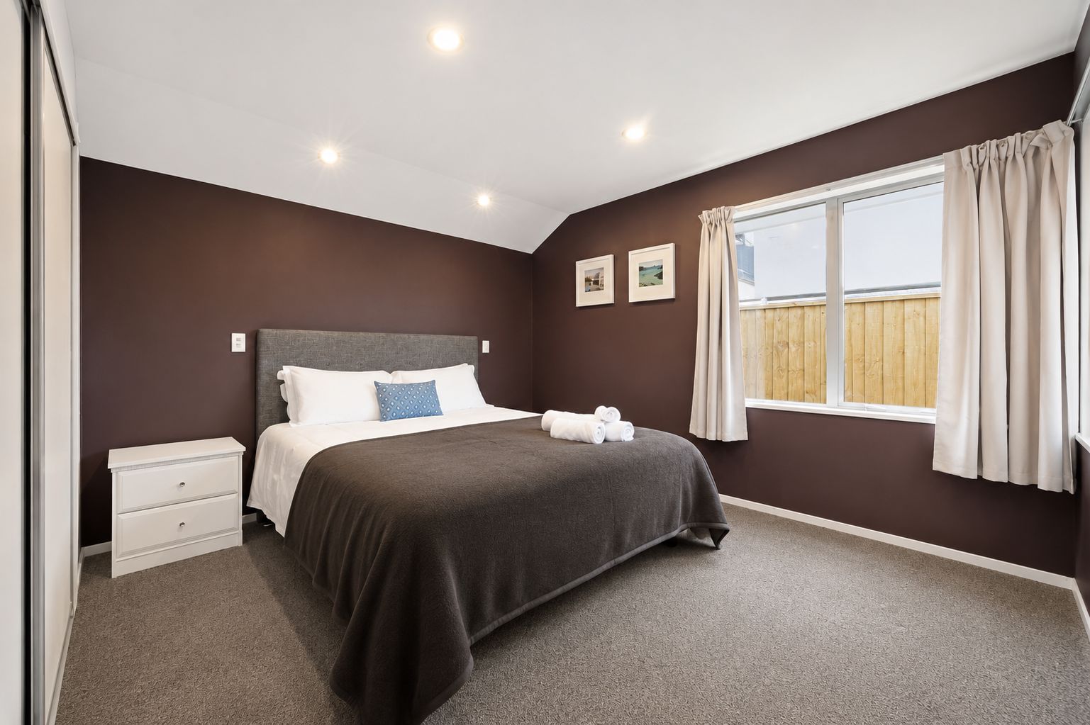 A bedroom with a bed, bedside tables, a window with curtains, and a view of the outside.