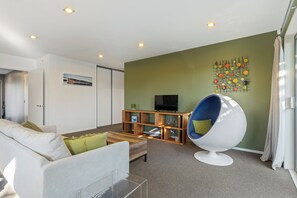 A modern living room with a sofa, a coffee table, a television, and a unique egg-shaped chair. - The Wild Fern by Aotearoa Escapes (Christchurch)