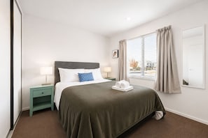 A hotel room with a bed, a nightstand, a window with curtains, and a view of the outside.