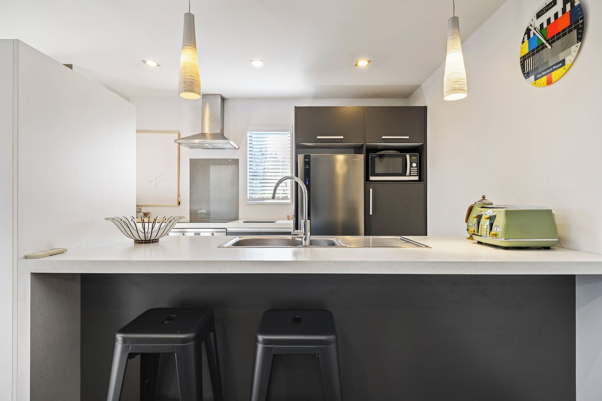 A modern kitchen with stainless steel appliances, a white countertop, and bar stools.