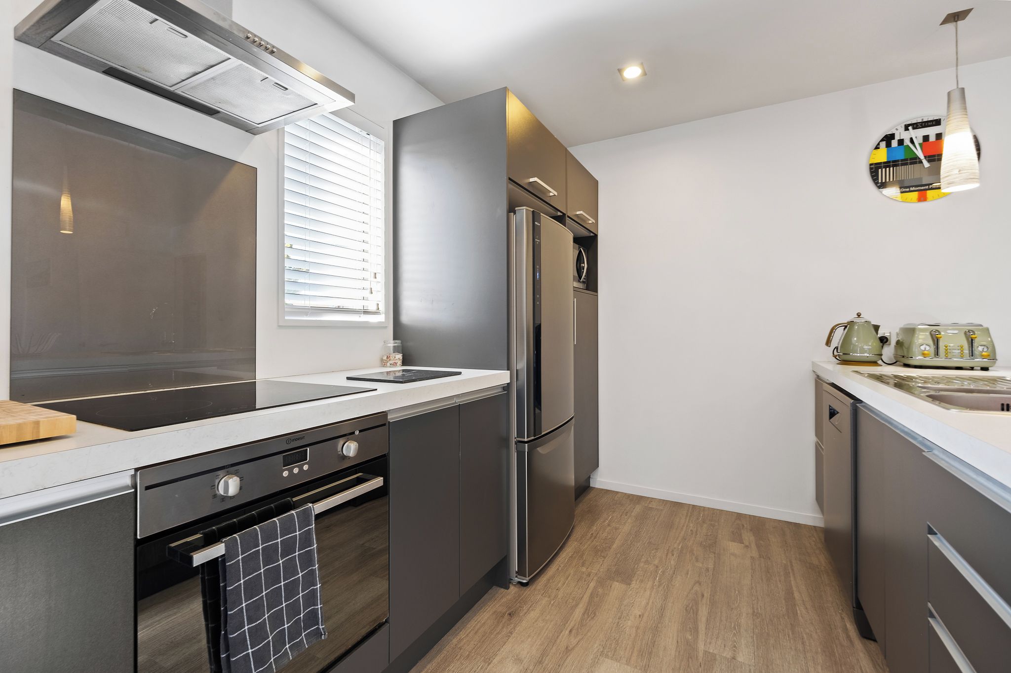 A modern kitchen with a built-in oven, a stainless steel refrigerator, and a window with blinds.