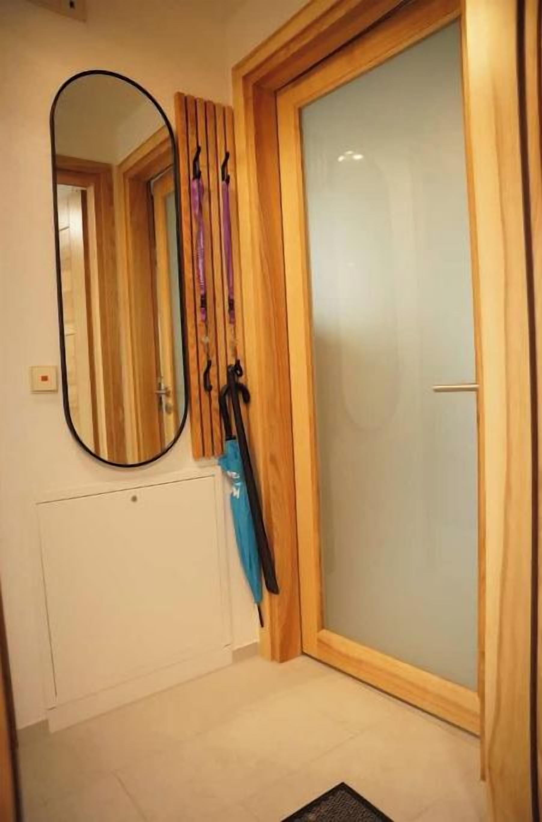 Una habitación con una puerta de madera, un espejo y un perchero con un objeto azul.