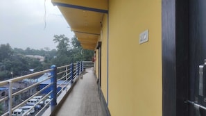 A corridor with a yellow wall, a blue railing, and a view of parked cars and trees.