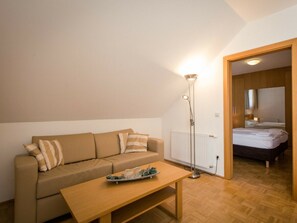 Una habitación acogedora con sofá, una mesita, una lámpara de pie y una cama al fondo.