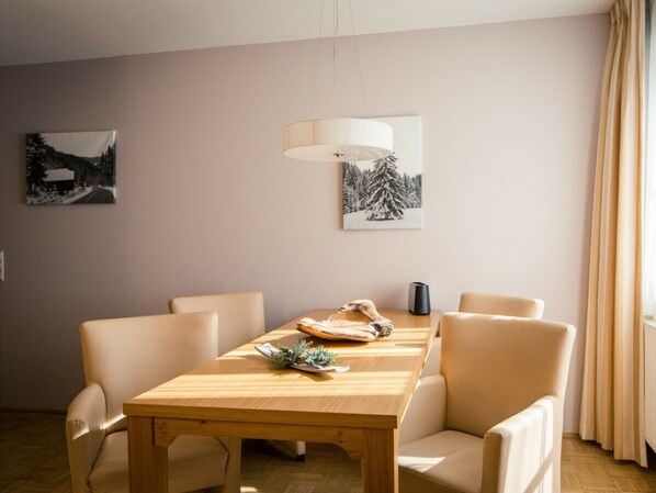 Un comedor con una mesa de madera, cuatro sillas, una lámpara y dos cuadros en la pared.
