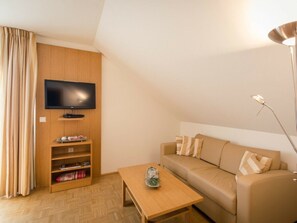 Un salon avec un téléviseur à écran plat fixé à un mur en bois, un canapé avec des coussins à rayures, une table basse en bois et un lampadaire.
