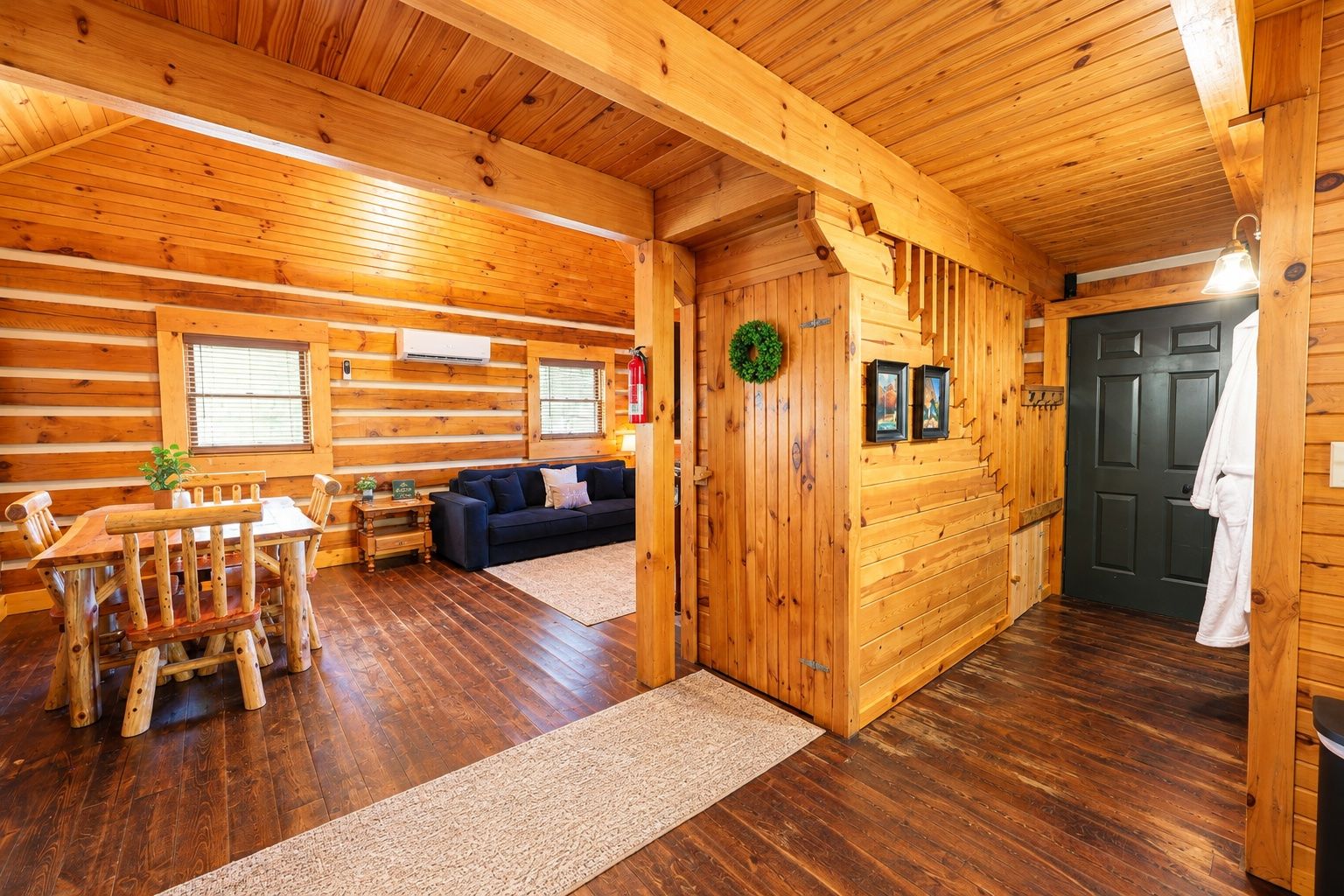 A log cabin interior with a dining area, sofa, and a staircase leading to a door.