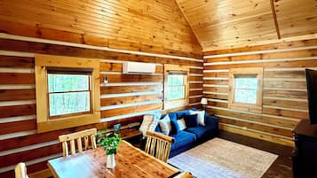A log cabin interior with a dining area, a sofa, and a ceiling fan.