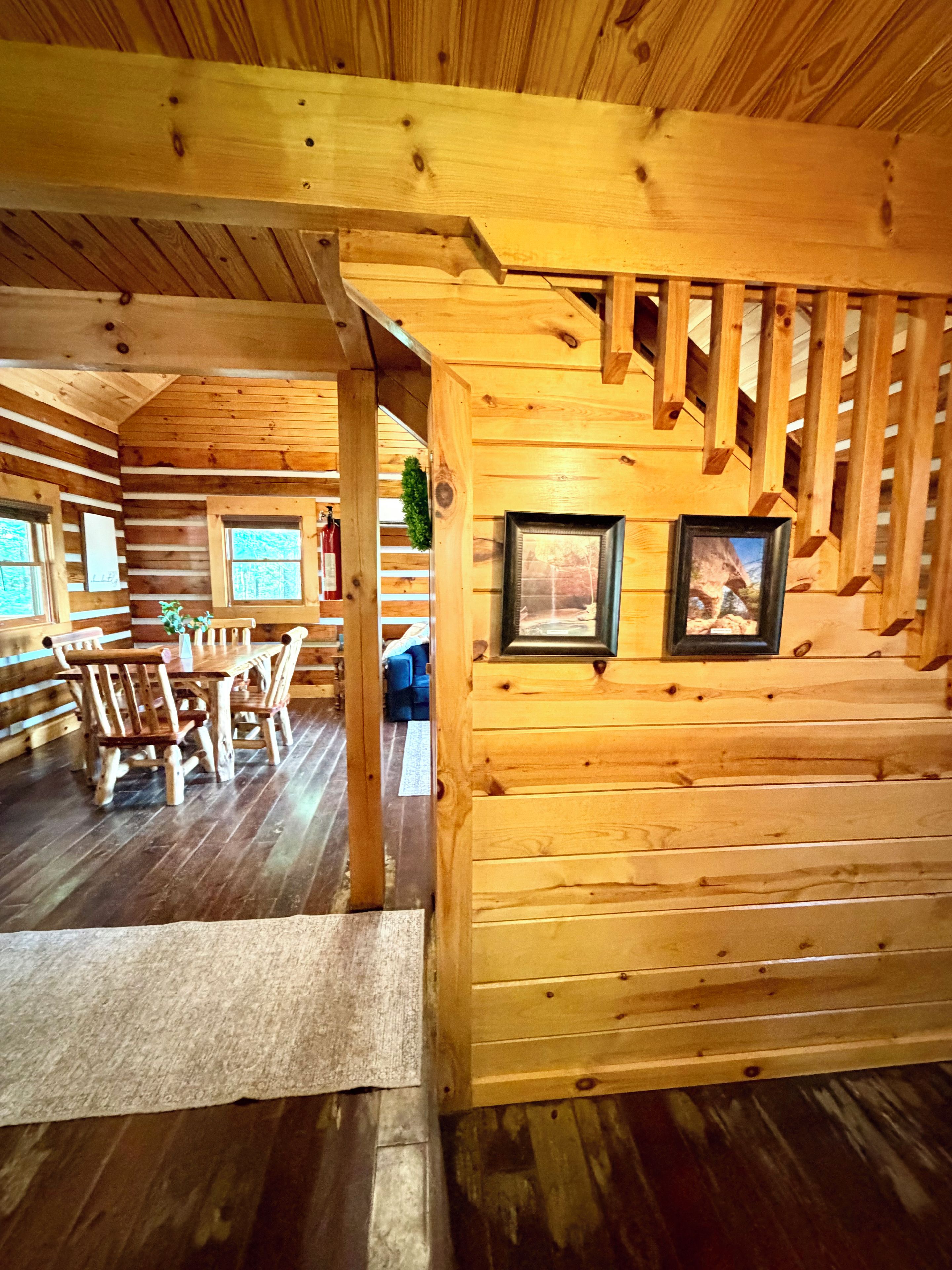 L’intérieur d’un chalet en bois comprend un coin repas, un escalier et des tableaux encadrés accrochés aux murs.