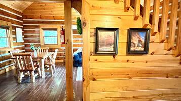 L’intérieur d’un chalet en bois comprend un coin repas, un escalier et des tableaux encadrés accrochés aux murs.
