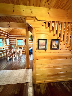 L’intérieur d’un chalet en bois comprend un coin repas, un escalier et des tableaux encadrés accrochés aux murs.