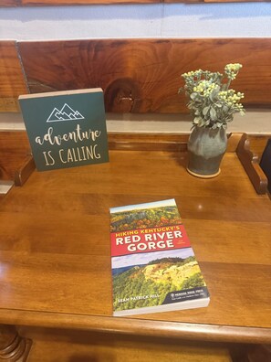 Une table en bois sur laquelle est posé un livre intitulé « Randonnées dans les gorges de Red River, Kentucky », et une pancarte sur laquelle on peut lire : « L’aventure vous appelle ».