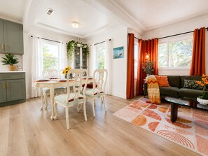 Ein Essbereich mit Tisch und Stühlen, einer Couch und einem Fenster mit Vorhängen.