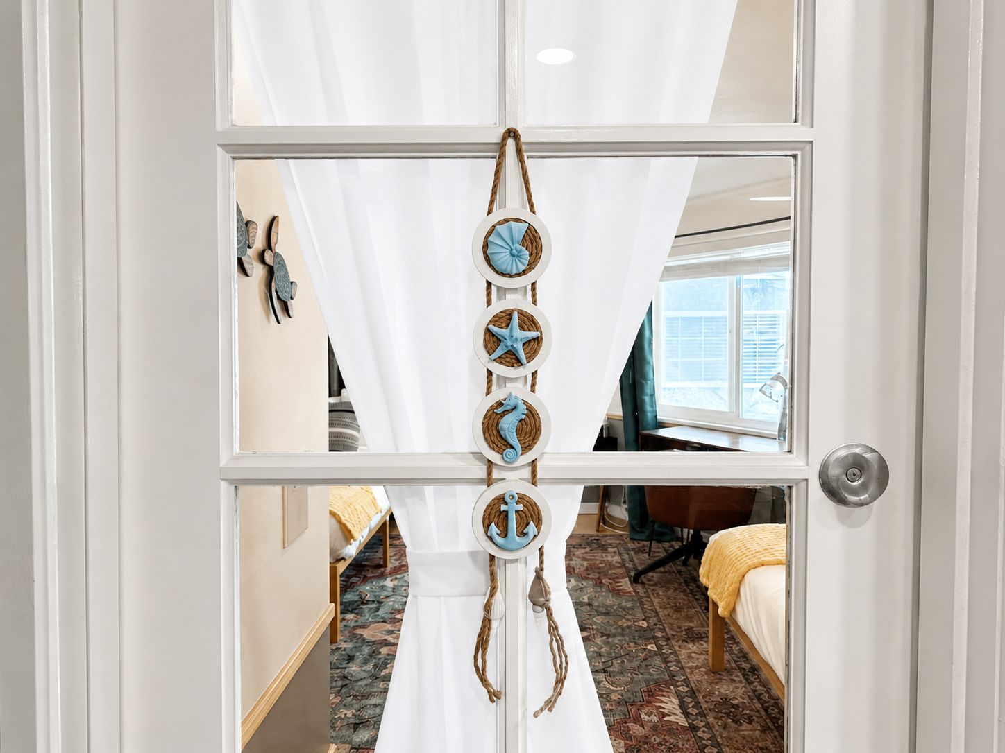 A room with a bed, a window, and a door with a decorative rope and starfish decoration.