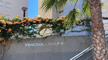 Ein Gebäudeeingang mit einem Schild, das 'Venezio Golf II' zeigt, und einer Palme im Vordergrund.