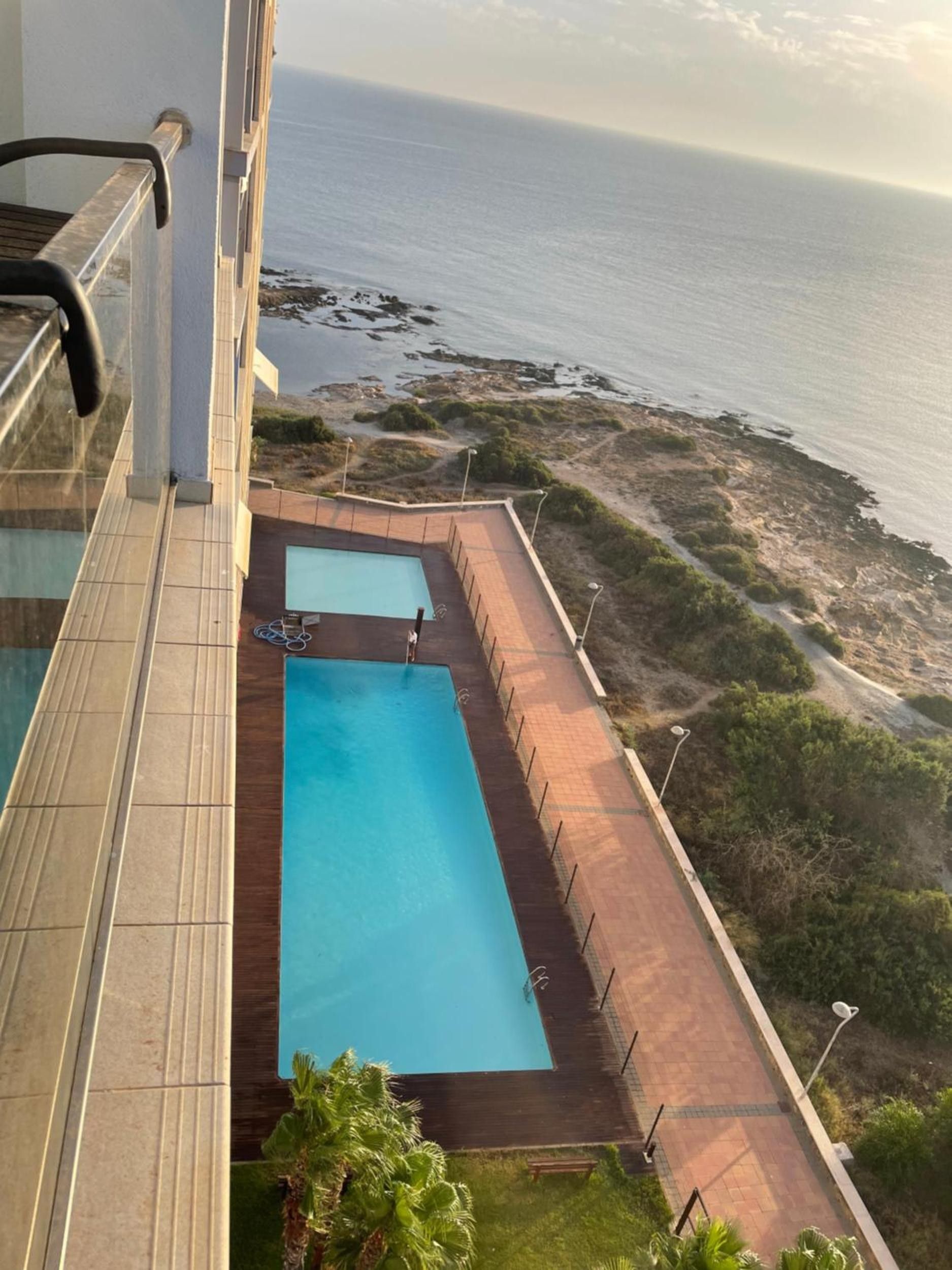 Ein Pool mit Blick auf den Ozean, umgeben von einer Holzterrasse und einem Pflasterweg.