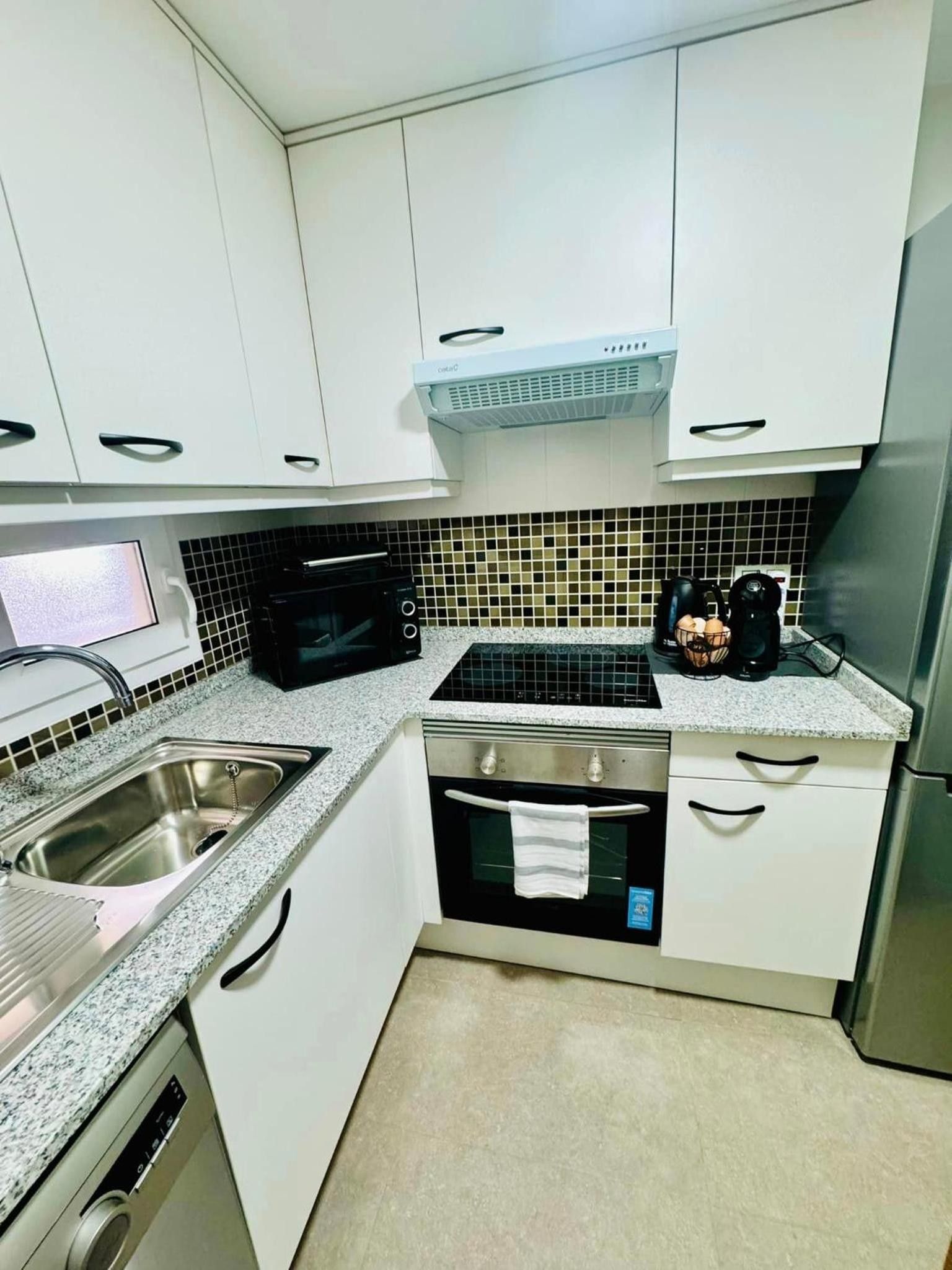 Een keuken met witte kasten, een zwarte magnetron, een roestvrijstalen spoelbak en een ingebouwde oven.
