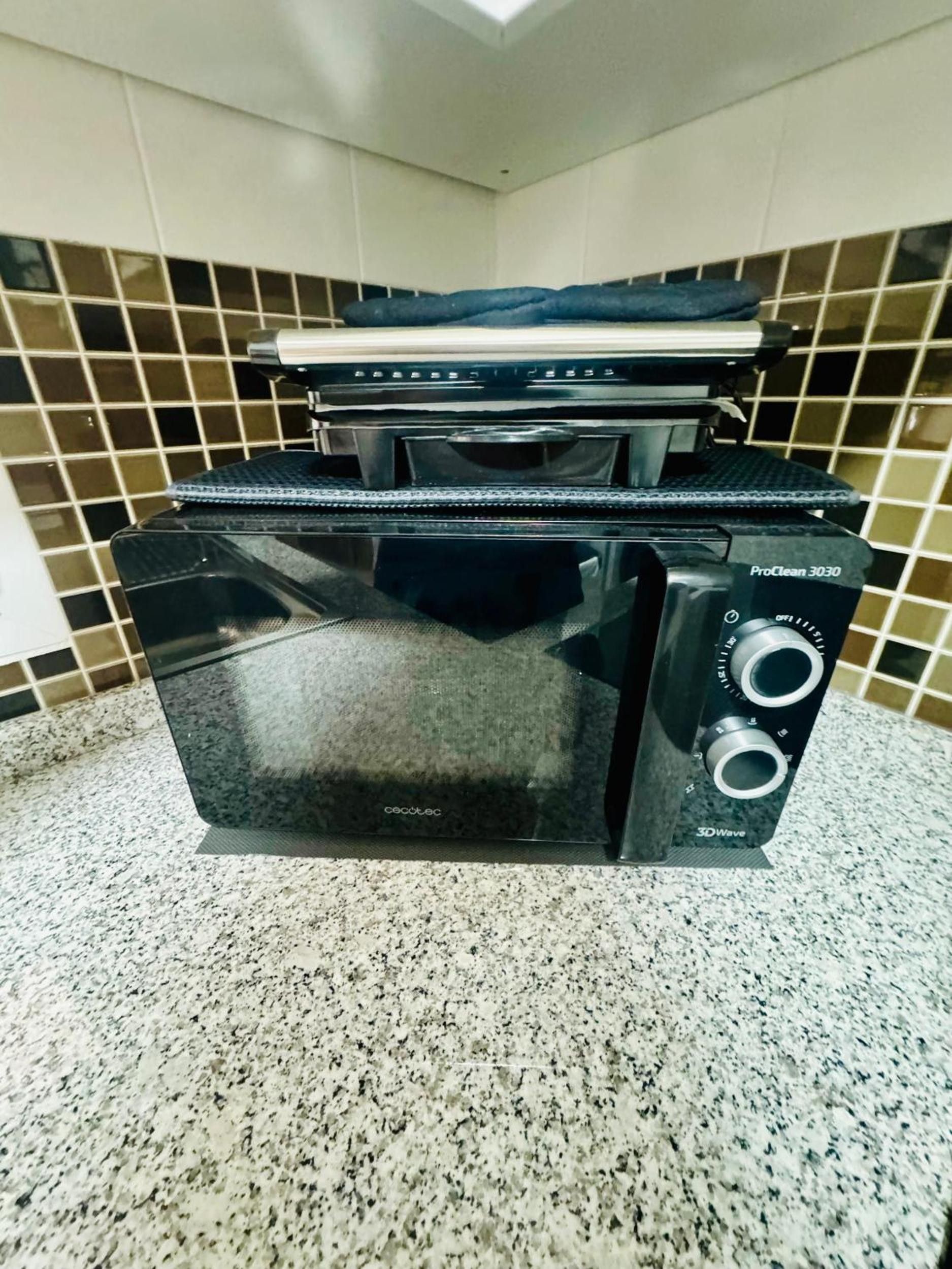 A black microwave oven with a digital display and control panel, placed on a granite countertop.