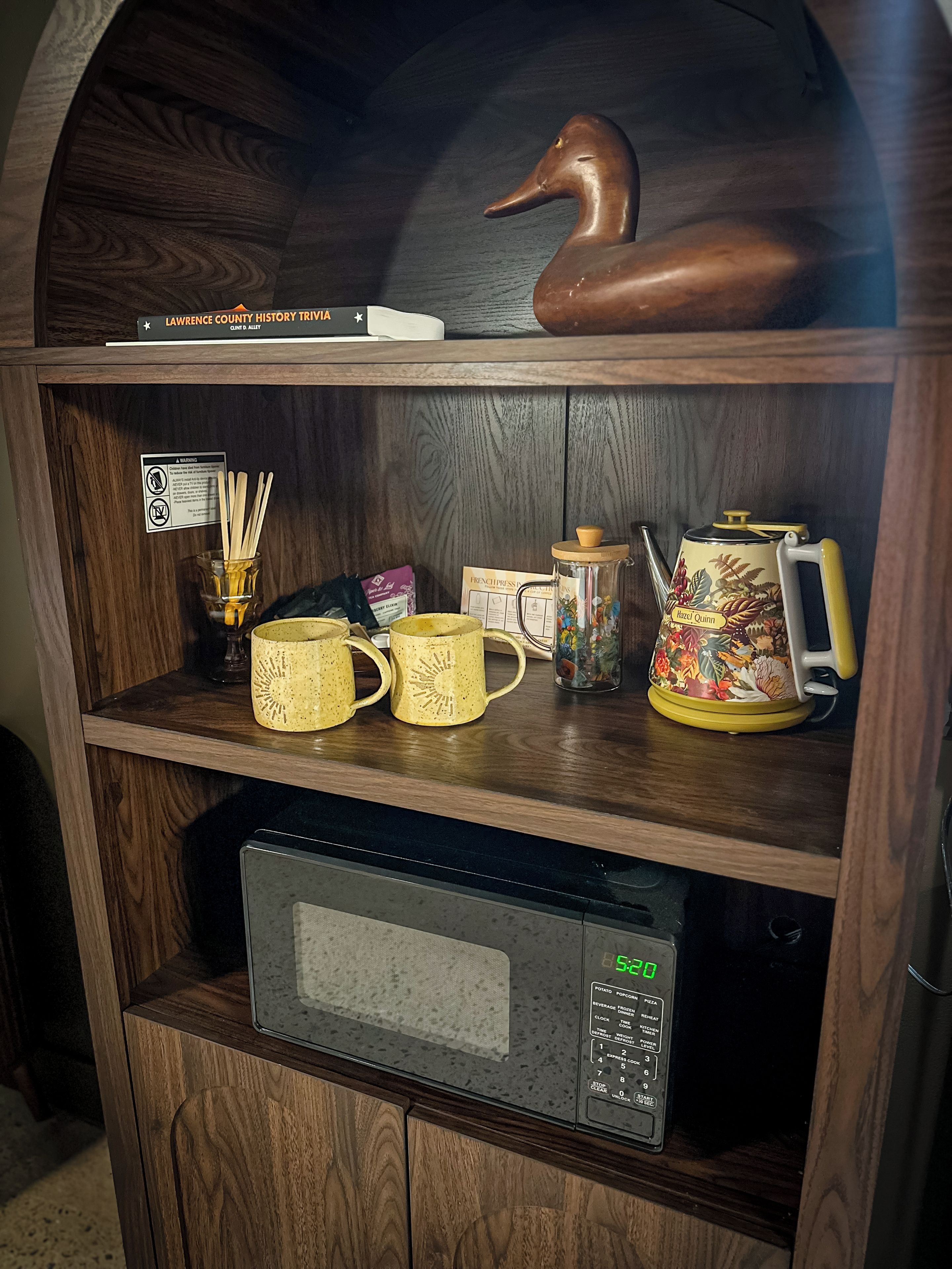 A wooden shelf with a duck figurine, a book titled 'Lawrence County History Trivia,' and a coffee maker.