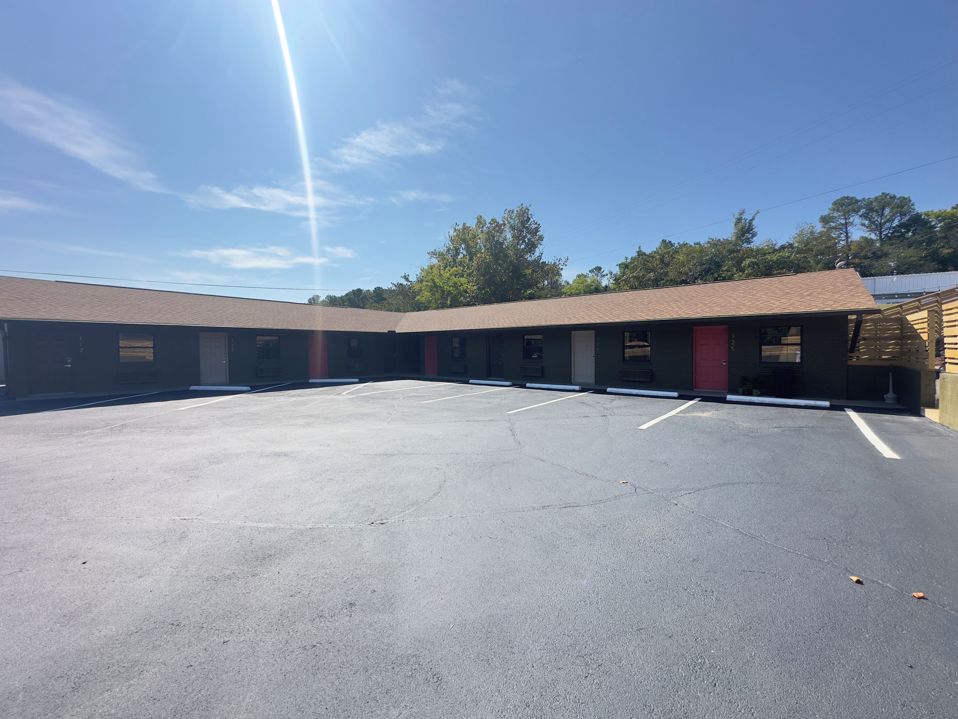 Un motel con un estacionamiento central, habitaciones individuales con puertas rojas y fachada de ladrillo.