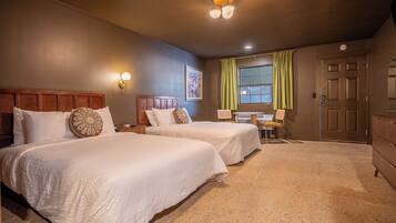 A hotel room with two beds, a desk, a chair, a window with curtains, and a door.
