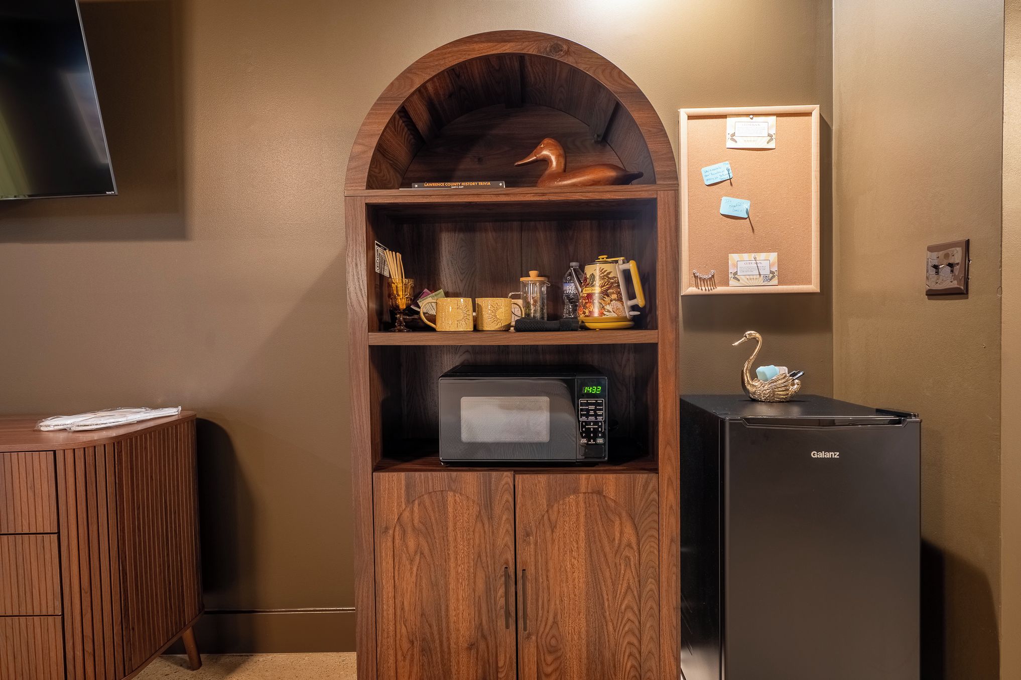 A kitchenette with a microwave, refrigerator, and wooden cabinet with decorative items.