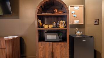 A kitchenette with a microwave, refrigerator, and wooden cabinet with decorative items.