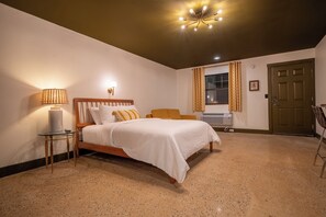 A bedroom with a bed, a nightstand, a lamp, a window with curtains, and a door.