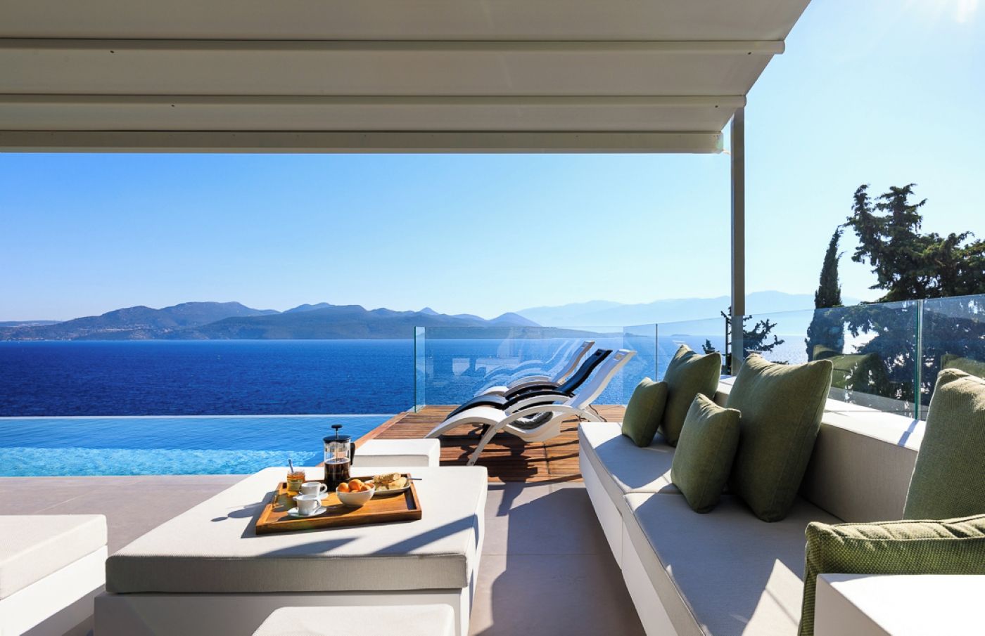A sunlit outdoor seating area with a view of the sea and mountains.