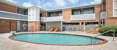 A swimming pool with lounge chairs and a brick building with balconies.