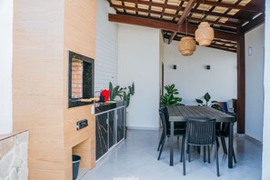 A patio area with a wooden table and chairs, a brick oven, and hanging wicker lamps.