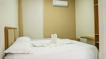 A hotel room with a bed, a wooden headboard, a bedside table, a nightstand, a wardrobe, and an air conditioning unit on the wall.