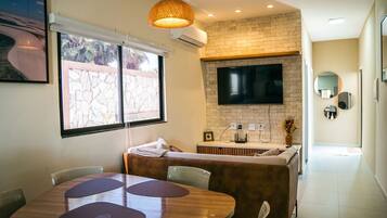 A modern kitchen with a brick wall, a flat-screen TV, and a dining area with a round table and chairs.