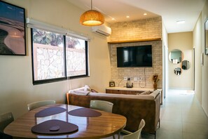 A modern kitchen with a brick wall, a flat-screen TV, and a dining area with a round table and chairs.