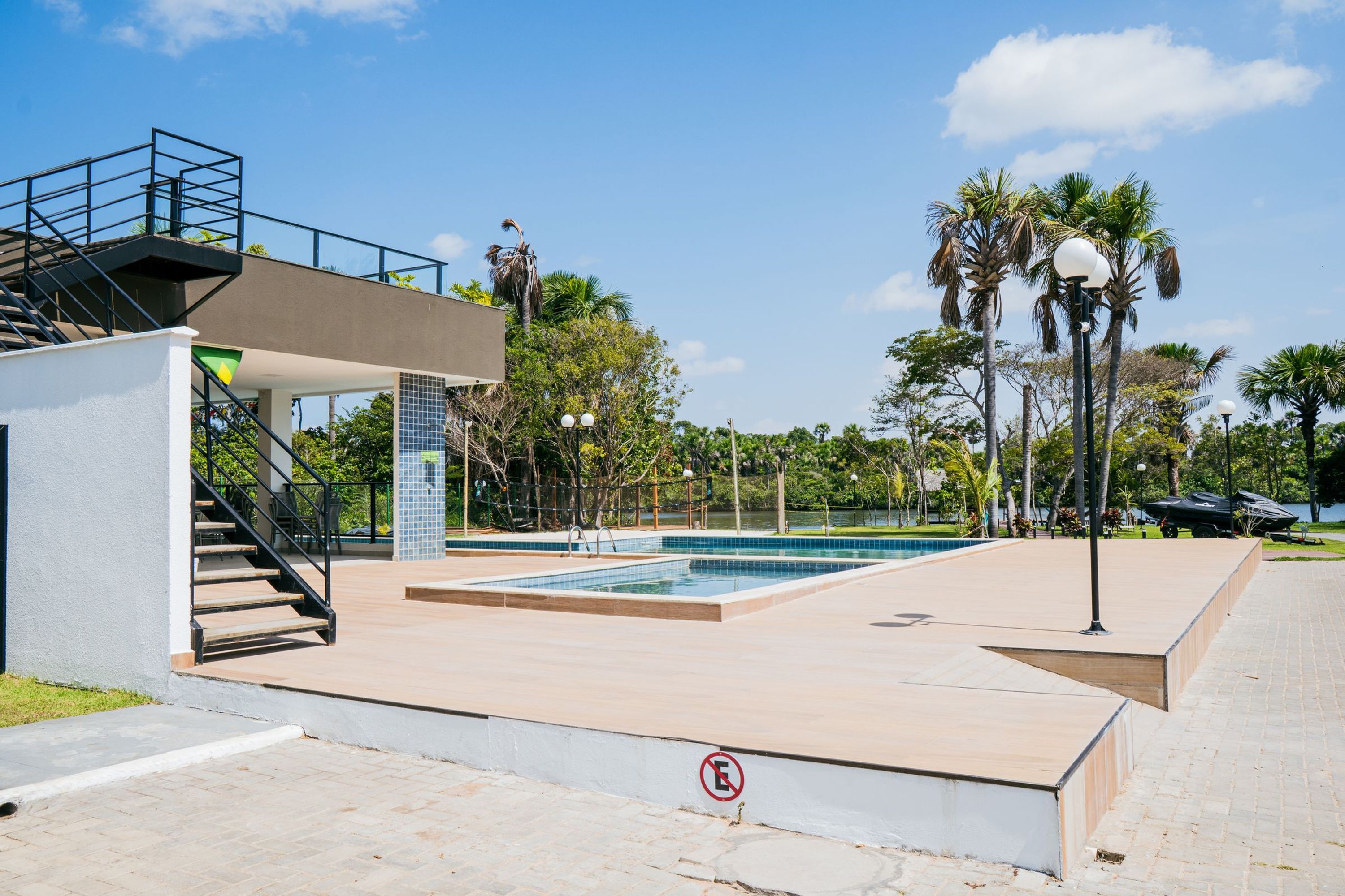 A swimming pool area with a staircase leading to an upper deck, surrounded by palm trees and a clear sky.