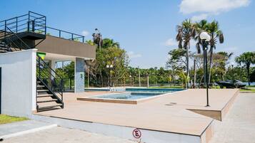A swimming pool area with a staircase leading to an upper deck, surrounded by palm trees and a clear sky.
