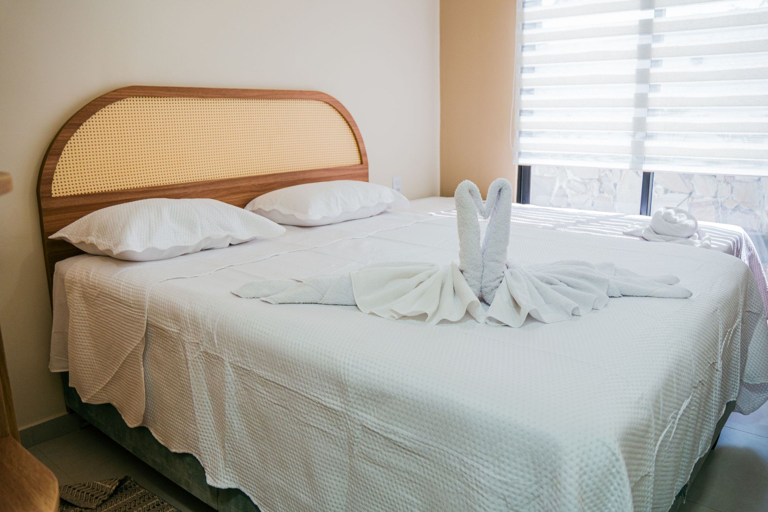 Un lit bien fait, avec un couvre-lit blanc et des oreillers, une tête de lit en bois et des serviettes disposées sur le lit.