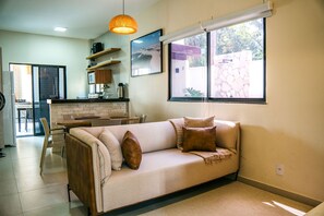 Una sala de estar con un sofá, una mesa de centro y un comedor con sillas. Se ve una cocina al fondo.