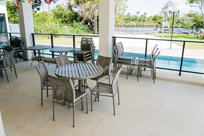 A covered outdoor seating area with tables and chairs, overlooking a swimming pool and a view of the surrounding greenery.