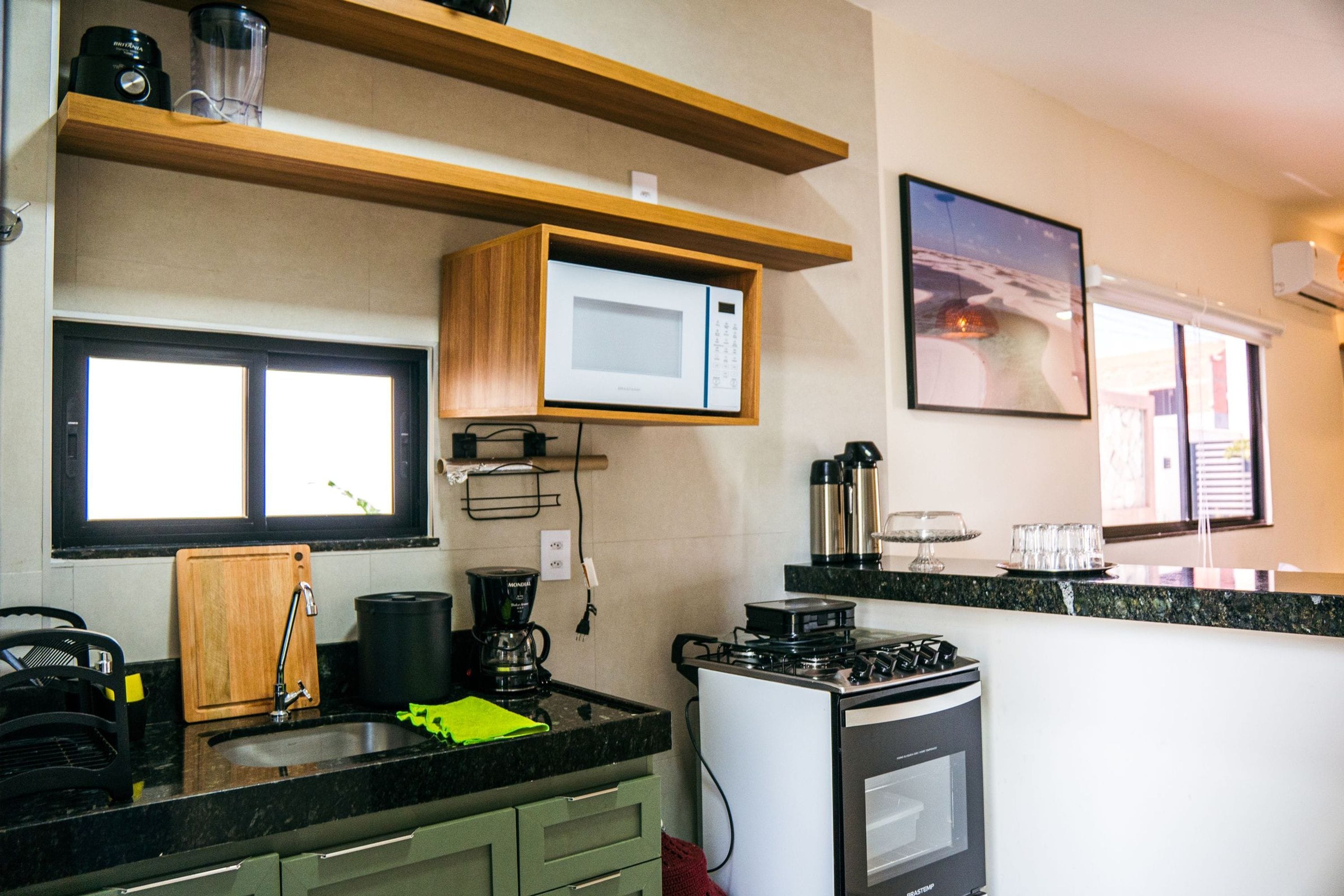 Una cocina compacta con microondas, cafetera y estufa. Hay una ventana con persianas, un lavamanos y una encimera.