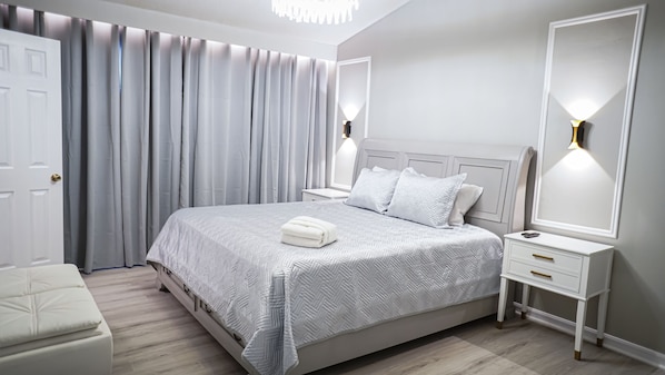 A bedroom with a large bed, bedside tables, a nightstand, a chair, and a door.