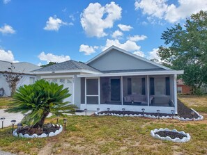 A single-story house with a covered porch, a large window, and a well-maintained lawn with a palm tree.