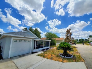 A residential property with a garage, a covered porch, and a landscaped garden with a palm tree.